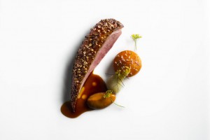 Roasted duck with thyme roasted apricot, apricot puree, and fennel with apricot jus on a white surface. Prepared by Daniel Humm at Eleven Madison Park.